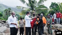 Presiden Joko Widodo (tengah) memberikan jaketnya kepada seorang korban saat memeriksa kerusakan di Pulau Lembata akibat hujan lebat dari Siklon Tropis Seroja, 9 April 2021. (Istana Presiden RI/AFP)
