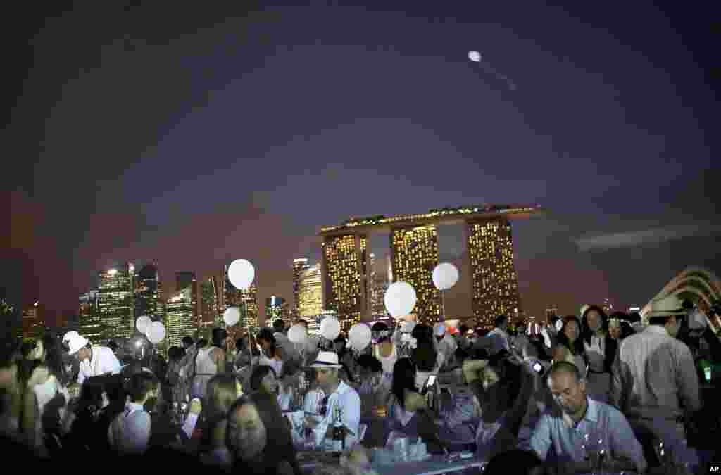 Guests sit at dinner tables set up with the Marina Bay Sands and the financial skyline as a backdrop at the Marina Barrage in Singapore. Diner en Blanc or "White Dinner" which started in Paris 25 years ago, is into its second year in Singapore. The guests are expected to dress in only white and bring their own food, tables and chairs for a fine dining flash mob style gathering in a secret location made known to them only minutes before the event.