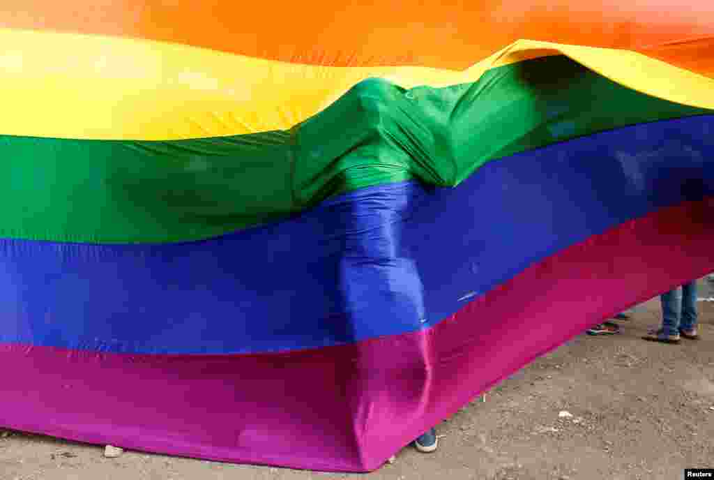 یک شرکت کننده در یادبود قربانیان حمله به کلوب همجنسگراها در اورلاندو، پشت پرچم رنگین کمانی همجنسگراها.