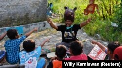 Samsudin mengenakan topi berbentuk kuda nil memainkan boneka-boneka tentang hewan-hewan endemik di Indonesia saat mendongeng untuk anak-anak di Indramayu, Jawa Barat, 12 Maret 2021. (Foto: Willy Kurniawan/Reuters)