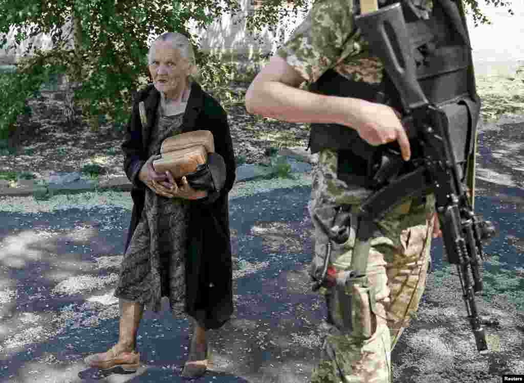 Một người dân địa phương cầm những ổ bánh mì đi ngang qua một binh sĩ Ukraine đứng gác ở làng Novotoshkivske gần tiền tuyến với quân ly khai thân Nga, miền đông Ukraine.