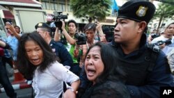 A woman tries to help as an anti-coup protester is detained by a Thai police officer during a street protest in Bangkok, Thailand, on May 24, 2014.