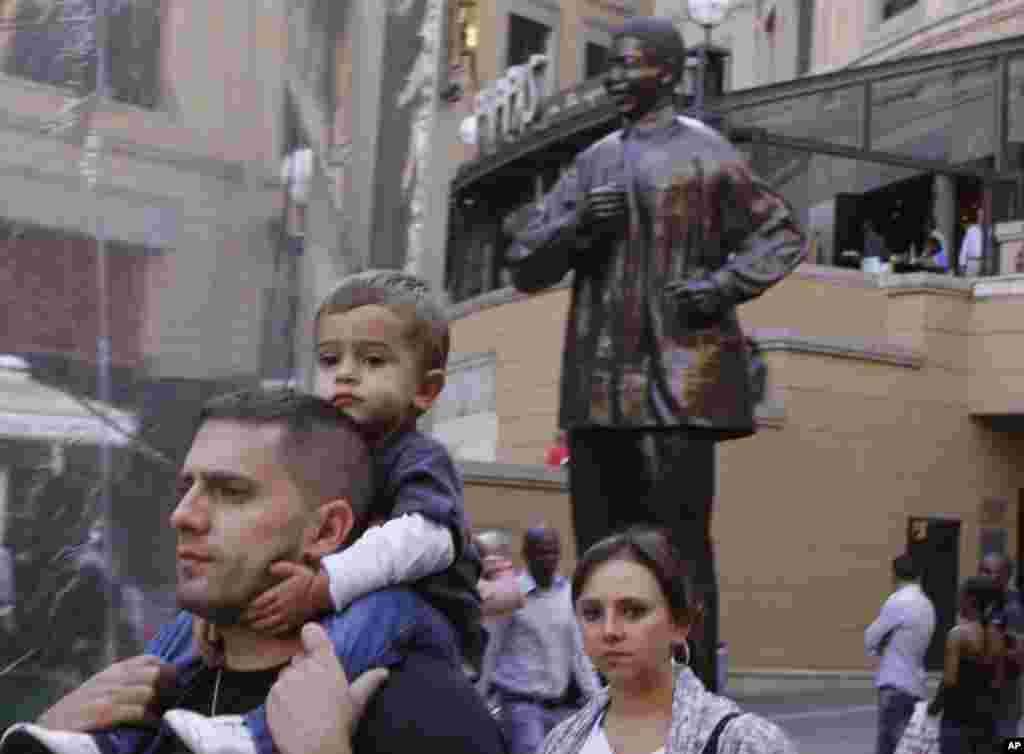Visitors to Nelson Mandela Square in Johannesburg pass beneath a statue of the former president, April 1, 2013.