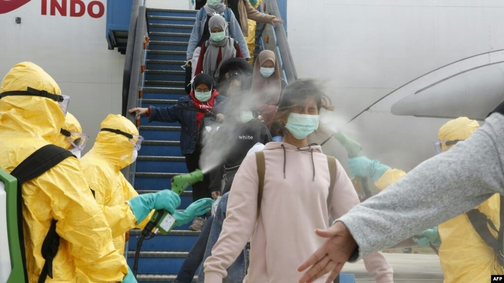 This handout photo taken and released by the Indonesian Embassy on February 2, 2020, shows officials in full protective gear disinfecting Indonesian students as they disembark upon the arrival at Hang Nadim international airport in Batam.