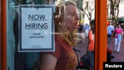 FILE - A woman walks past a 'Now Hiring' sign as she leaves the Urban Outfitters store at Quincy Market in Boston, Massachusetts. 