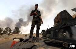 A member of the Iraqi government forces stands on a military vehicle as smoke billows from oil wells, set ablaze by Islamic State (IS) group militants before fleeing the oil-producing region of Qayyarah, Aug. 30, 2016.