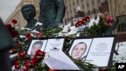 Photos of Lt.Col. Oleg Peshkov, left, and sailor Alexander Pozynich are placed at a monument to Soviet Officers with flowers and a toy jet made of paper outside Russian Army General Staff headquarters in Moscow, Nov. 26, 2015.