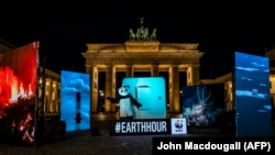 Seorang aktivis LSM World Wide Fund for Nature (WWF) mengenakan kostum panda bersiap mematikan saklar raksasa untuk mematikan lampu-lampu di Gerbang Brandenburg di Berlin, dalam peringatan Earth Hour, di Berlin, Jerman, 27 Maret 2021. (Foto: John Macdouga