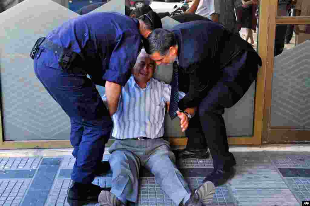 A crying elderly man is assisted by an employee and a policeman outside a national bank branch as pensioners queue to get their pensions, with a limit of 120 euros, in Thessaloniki, Greece.