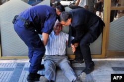 Một nhân viên và một cảnh sát trợ giúp một người đàn ông đang khóc bên ngoài một ngân hàng quốc gia trong khi người dân xếp hàng nhận lương hưu với giới hạn là 120 euro ở Thessaloniki, 3/7/2015.