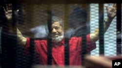 FILE - Former Egyptian President Mohamed Morsi, wearing a red jumpsuit that designates he has been sentenced to death, raises his hands inside a defendants cage in a makeshift courtroom at the national police academy, in an eastern suburb of Cairo.
