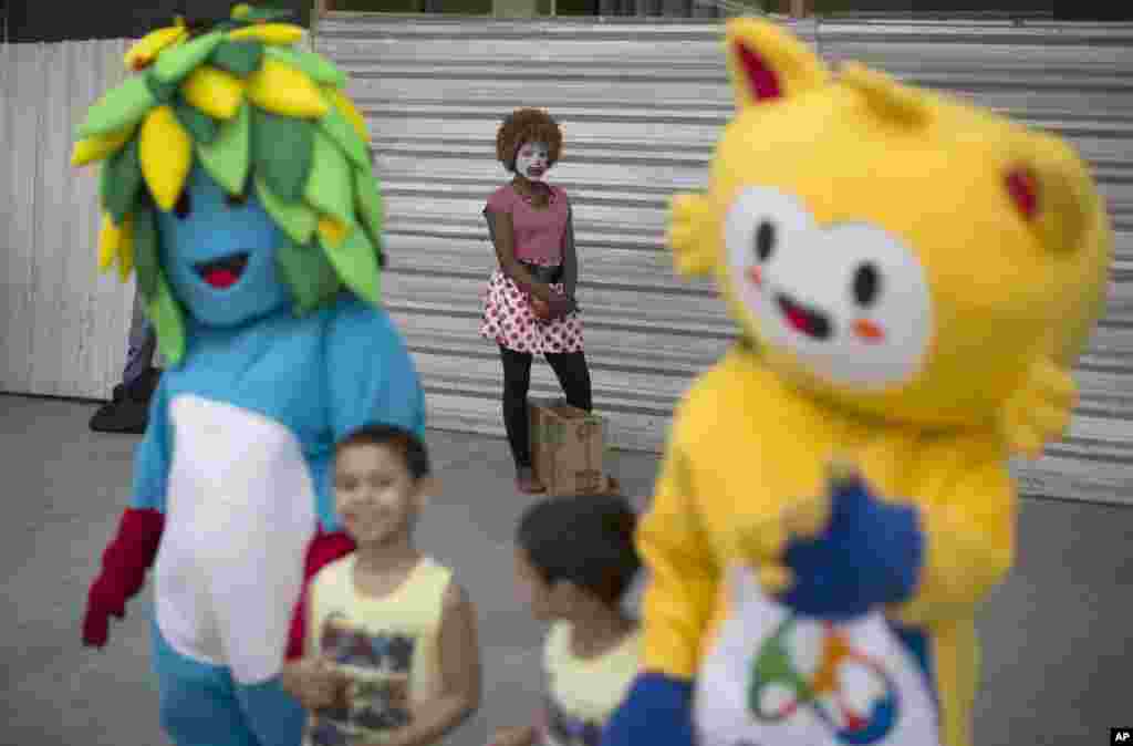 A clown stands next to spectators dressed as Olympic mascots as they wait for the Olympic torch on its way to Rio de Janeiro for the opening ceremony of Rio's 2016 Summer Olympics, in Niteroi, Brazil, Tuesday, Aug. 2, 2016. The three-month torch relay across Brazil will end at the opening ceremony on Aug. 5, in Maracana stadium. (AP Photo/Leo Correa)