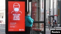 Seorang wanita yang memakai masker sedang menunggu di halte bus di London,Inggris, 18 Mei 2020. (Foto: REUTERS/Simon Dawson)