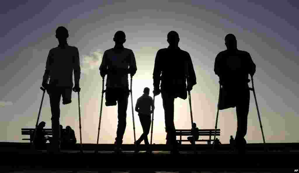Four Palestinian friends, who were injured during conflicts, walk by the sea at Gaza's small fishing harbor.