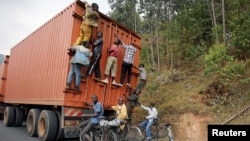 FILE - Young people on bicycles hang to the back of a truck July 19, 2015, outside the capital Bujumbura, Burundi.