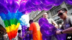 Kajsa Westman, second from right, of Stockholm, Sweden, and Victor Ng, right, of Seattle, tie balloons to a banner in preparation for the annual Gay Pride parade, file photo. 