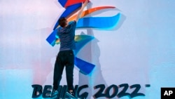 FILE - A crew member fixes a logo for the 2022 Beijing Winter Olympics before a launch ceremony to reveal the motto for the Winter Olympics and Paralympics in Beijing on Sept. 17, 2021. 