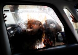 Para aktor yang berdandan seperti zombie dan hantu dalam pertunjukan rumah hantu oleh kelompok Kowagarasetai, untuk para pengunjung di dalam mobil di tengah imbauan menjaga jarak aman untuk mencegah penularan Covid-19 di Tokyo, 3 Juli 2020. (Foto: Reuters