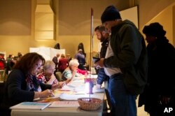 FILE - An election official, left, checks the ID of a voter lining up to cast a ballot at a polling site for the New Hampshire primary in Nashua, Feb. 9, 2016.