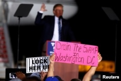 A man holds up a "Drain the Swamp in Washington DC" sign as then-Republican presidential nominee Donald Trump attends a campaign event on the tarmac of the airport in Kinston, North Carolina, Oct. 26 2016.