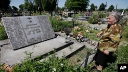 FILE - A woman stands near a mass grave and a monument in the village of Chlaniow, Poland, that holds the bodies of Poles killed in a 1944 attack on the village by the Nazi SS-led Ukrainian Self Defense Legion, June 19, 2013.