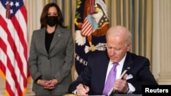 Presiden AS Joe Biden menandatangani perintah eksekutif, disaksikan oleh Wapres Kamala Harris, di Gedung Putih (26/1). 