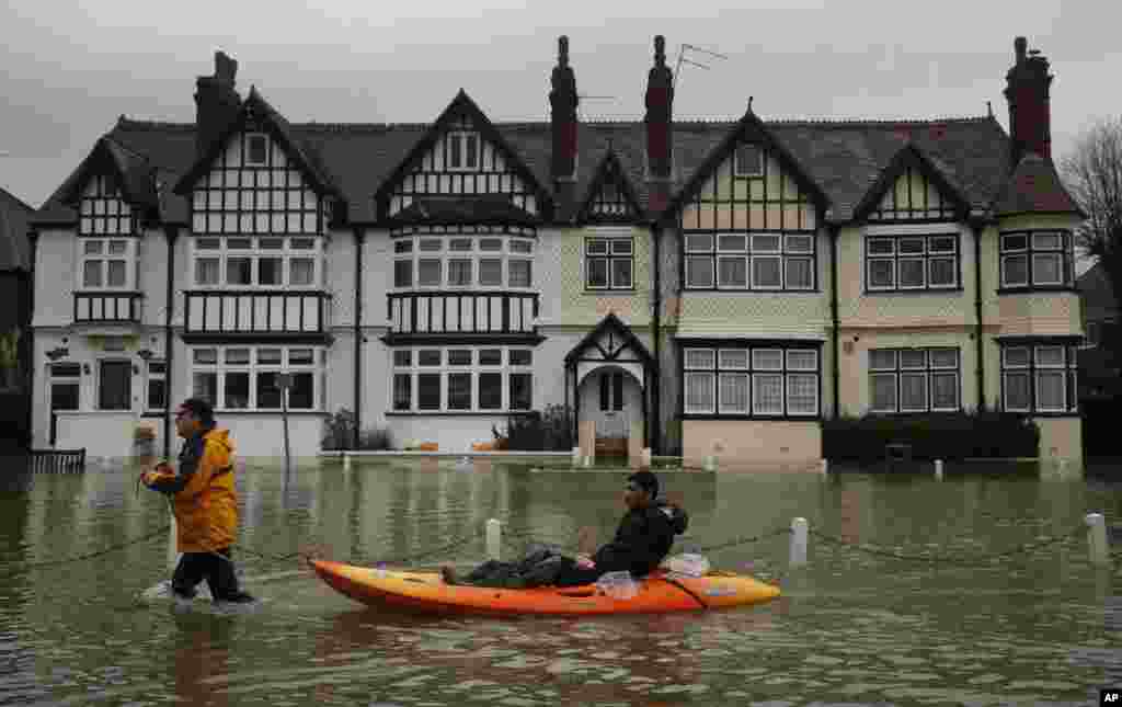 A man sits in a boat pulled by another man through a flooded street, in the center of the village of Datchet, England. The River Thames has burst its banks after reaching its highest level in years, flooding riverside towns upstream of London.
