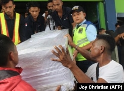 Ambrosius Koa (depan Kanan), kerabat TKI Adelina Sau, PRT yang meninggal di Malaysia, membantu petugas bandara menurunkan peti jenazahnya saat tiba di Bandara Kupang, Nusa Tenggara Timur pada 17 Februari 2018. (Foto: AFP/ Joy Christian))