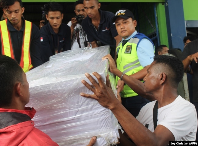 Ambrosius Koa (depan Kanan), kerabat TKI Adelina Sau, PRT yang meninggal di Malaysia, membantu petugas bandara menurunkan peti jenazahnya saat tiba di Bandara Kupang, Nusa Tenggara Timur pada 17 Februari 2018. (Foto: AFP/ Joy Christian))