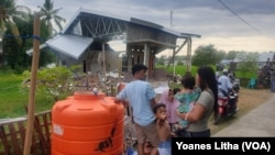 Warga sedang mengantri mengakses air bersih dari sebuah tandon air dengan latar rumah yang rusak berat akibat gempa di desa Banua, Kecamatan Malunda. Jumat (28/1/2021). (Foto: VOA/Yoanes Litha)