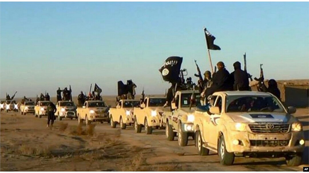 FILE - Militants of the Islamic State group hold up their weapons and wave flags on their vehicles in a convoy on a road leading to Iraq, while riding in Raqqa, Syria.