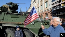 FILE - A man holding a U.S. flag walks past a U.S. Army Stryker armored vehicle, part of "Atlantic Resolve" NATO exercises, passing through Bialystok, Poland, March 24, 2015.