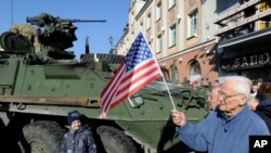 Чоловік із прапором США проходить повз американську бронемашину Stryker в м.Білосток, Польща. 24 березня 2015 року (AP Photo/Alik Keplicz)