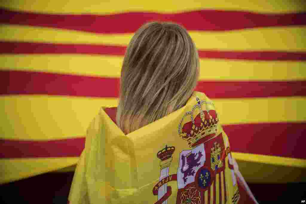 زنی که پرچم اسپانیا به دور خود بسته، پرچم منطقه کاتالونیا را نظاره می کند. جدایی طلبان پیشنهاد مذاکره را پذیرفته اند.