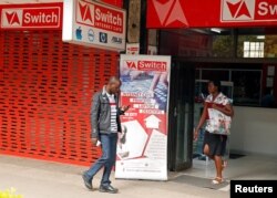 FILE - A man checks his mobile phone outside an internet cafe in Harare, Zimbabwe, Jan. 21, 2019.