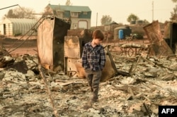 FILE - Jacob Saylors, 11, walks through the burned remains of his home in Paradise, Calif., Nov. 18, 2018. The family lost a home in the same spot to a fire 10 years prior.
