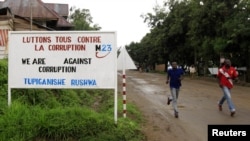 People jog past a sign, with a message by the M23 movement in their campaign against rampant corruption in the Democratic Republic of Congo, in an area under controlled of the Congolese Revolutionary Army (CRA) in Rutshuru town, November 3, 2012.