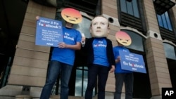 FILE - A protester wearing a mask with the face of Facebook founder Mark Zuckerberg is flanked by two fellow activists wearing angry face emoji masks, during a protest against Facebook policies, in London, Britain, April 26, 2018.