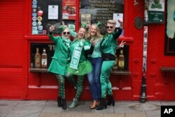 Sejumlah turis berpose di depan pub di Kota Dublin setelah pawai Santo Patrick dibatalkan untuk mencegah penyebaran virus corona, 17 Maret 2020. (Foto: AP)