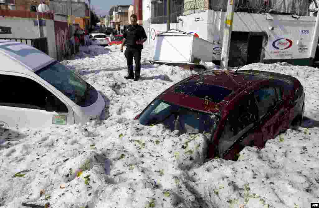 A policeman stands next to vehicles buried in hail in the eastern area of Guadalajara, Jalisco state, Mexico, June 30, 2019.