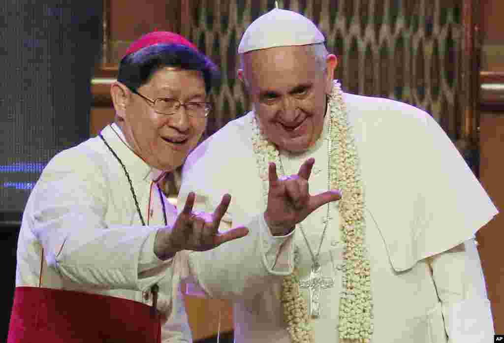 Kardinal Filipina Luis Antonio Tagle (kiri), memperlihatkan bagaimana membentuk simbul jari yang melambangkan &quot;Aku Cinta Kamu&quot; kepada Paus Francis di arena Mall Asia di Manila.&nbsp; Paus Francis mengadakan kunjungan apostolik selama lima hari di negara yang mayoritas penduduknya memeluk Katolik itu. &nbsp;