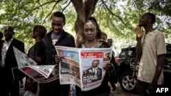 Supporters of the official DRCongo Presidential candidate, Emmanuel Ramazani Shadary, read a newspaper outside the Cathedral Notre-Dame Du Congo in Kinshasa, Nov. 24, 2018, during the launch of his official electoral campaign.