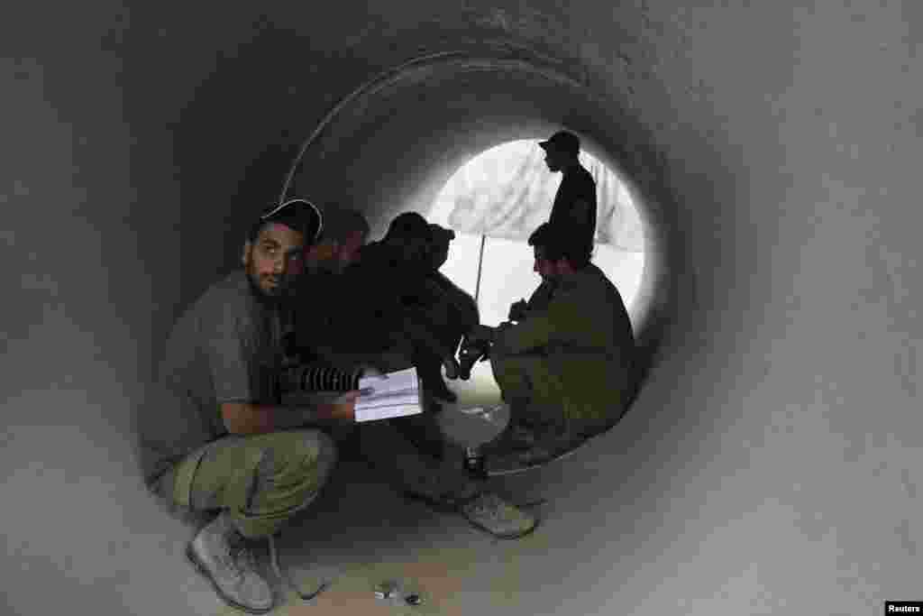 Israeli soldiers take cover in a concrete pipe, as a siren warning of incoming rockets sounds near the border with the Gaza Strip, August 4, 2014.