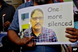 An Indian journalist participates in a silent protest against the brutal killing of a senior Kashmiri journalist Shujaat Bukhari, portrait seen, in Kolkata, India, June 15, 2018.