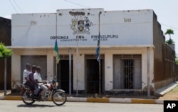 Men on a motorcycle pass the damaged administration headquarters in the town of Kasese, Uganda, Monday, Nov. 28, 2016.