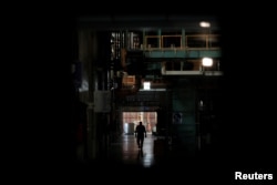 FILE - A worker walks next to halted machines at a cans' factory during a power cut in Valencia, Venezuela, April 8, 2019.