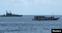 FILE - An Australian Navy boat, left, is positioned near a boat carrying 50 asylum seekers after it arrived at Flying Fish Cove on Christmas Island. The island's detention center for migrants was recently the scene of violent disturbances.