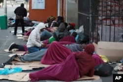 Refugees sleep on a sidewalk in Cape Town, South Africa, Friday, March 27, 2020, after South Africa went into a nationwide lockdown for 21 days in an effort to mitigate the spread to the coronavirus. (AP Photo/Nardus Engelbrecht)