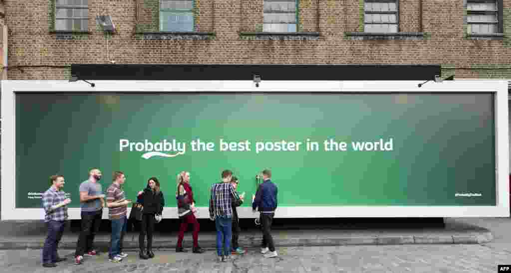 People line up by a billboard poster with a built in tap that is dispensing free beer outside the Truman Brewery in east London. The 12-meter billboard poster has been created by Carlsberg as part of its &#39;Probably the best beer in the world&#39; campaign.