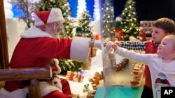 Julianna, 3, and Dylan, 5, Lasczak visit with Santa through a transparent barrier at a Bass Pro Shop in Bridgeport, Conn., Tuesday, Nov. 10, 2020. Santa Claus is coming to the mall — just don't try to sit on his lap. (AP Photo/Seth Wenig)